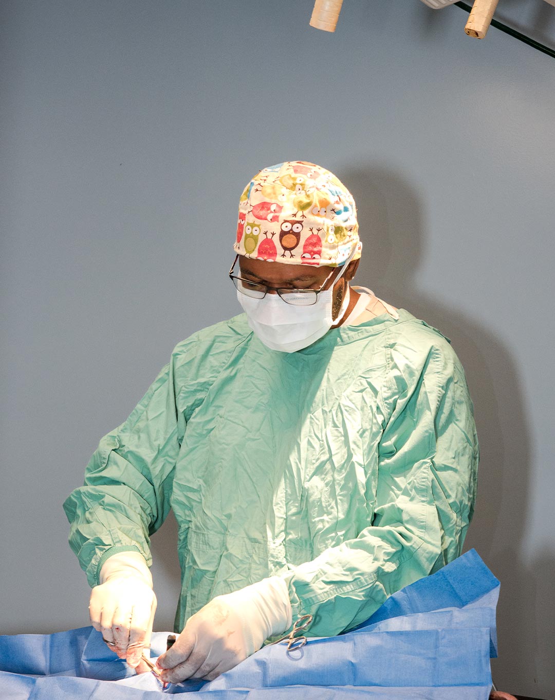 female veterinarian wearing a scrub cap with colorful owl pattern performing surgery